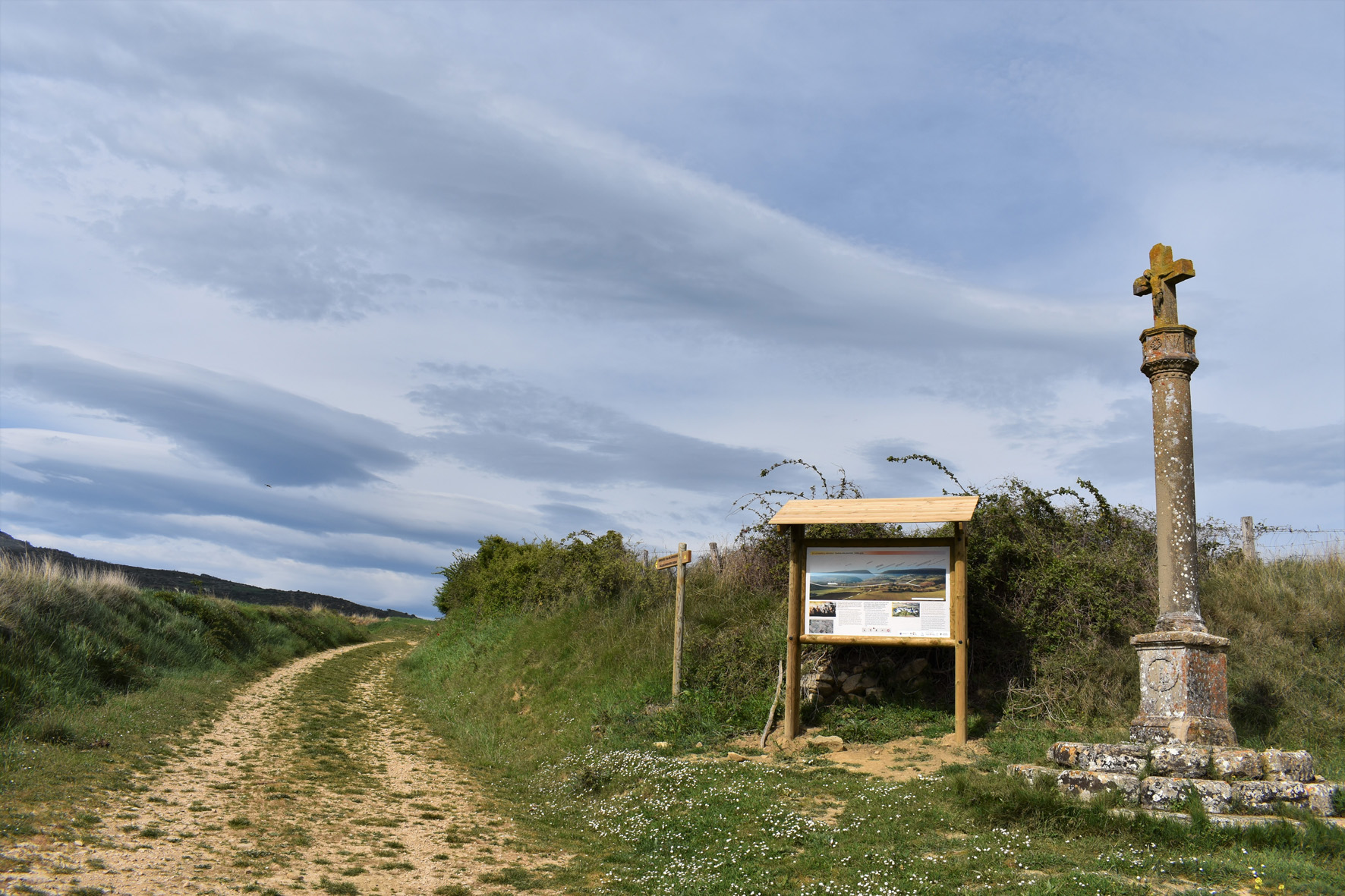 crucero de piedra y panel informativo en el borde del camino